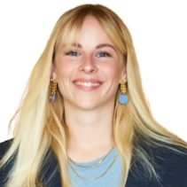 Face and shoulders of a smiling woman with straight long blonde hair, wearing a blue top, navy jacket, blue earrings and two gold chains, against a white background