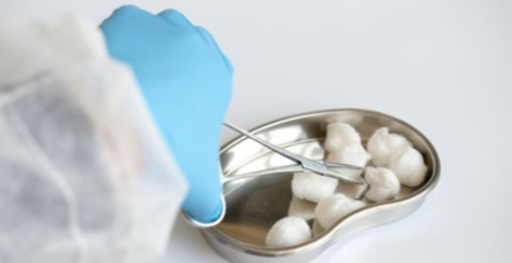 hand in medical glove using medical scissors on a metal dish of cotton balls