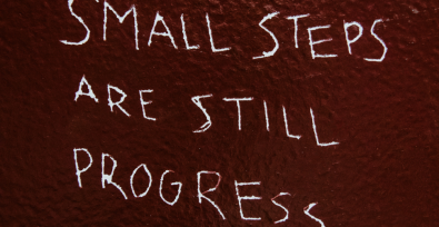 red wall with words in someones hand writing "small steps are still progress"