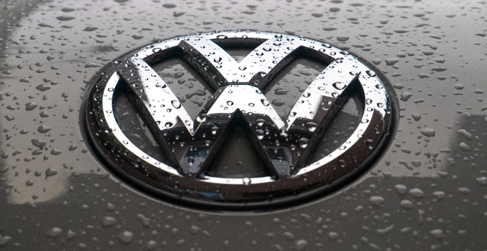 Logotipo de Volkswagen en plata sobre fondo gris con perlas de agua por encima.