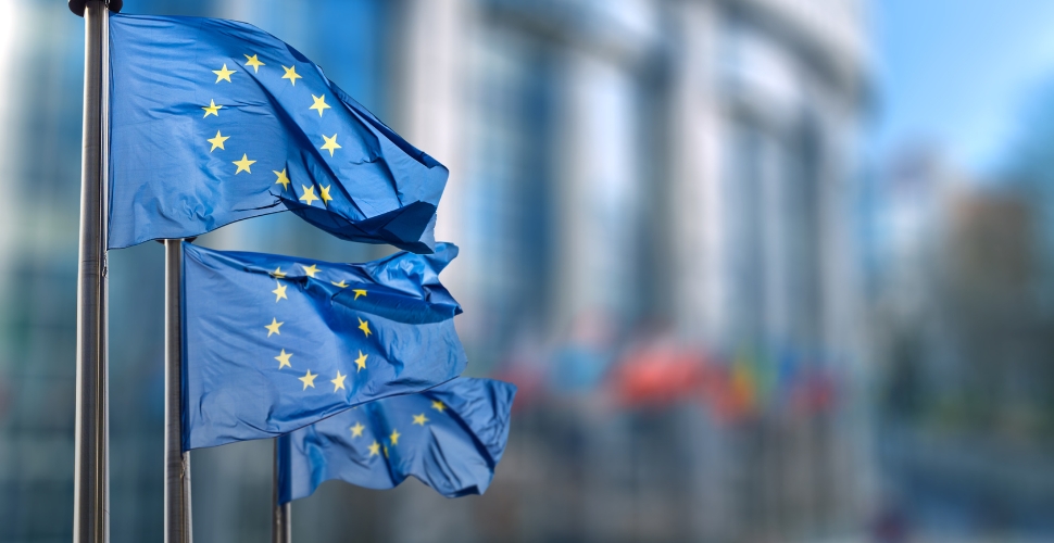 Three flags of the European Union in front of a blurry building in the background