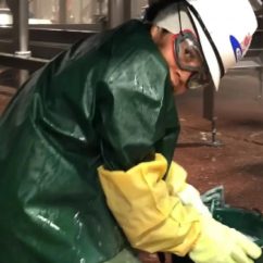 Young person in full workwear, including protective hat, googles, rubber gloves and waterproof coat crouching on the floor