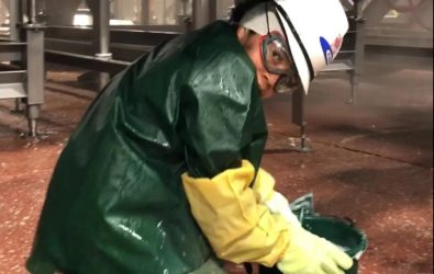 Young person in full workwear, including protective hat, googles, rubber gloves and waterproof coat crouching on the floor