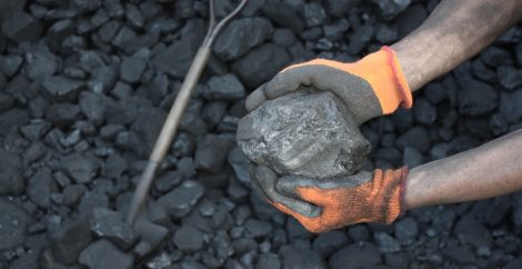 Two hands holding a large piece of mineral over more minerals with an axe in the background