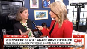 Captura de pantalla de la cobertura en vivo de CNN que muestra una vista lateral del presentador de cabello largo y rubio con una chaqueta roja sosteniendo un micrófono hacia la boca de una mujer de cabello castaño y chaqueta negra conversando.