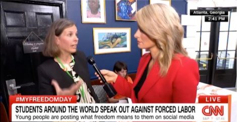 Screenshot from CNN live coverage showing a side view of the presenter with blond long hair wearing a red jacket holding a microphone toward the mouth of a woman with brown hair and a black jacket in conversation.