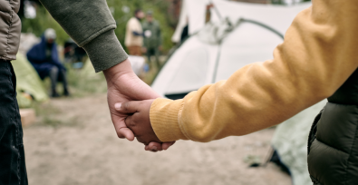 Two children holding hands, only their hands and arms are shown. Tent in the background