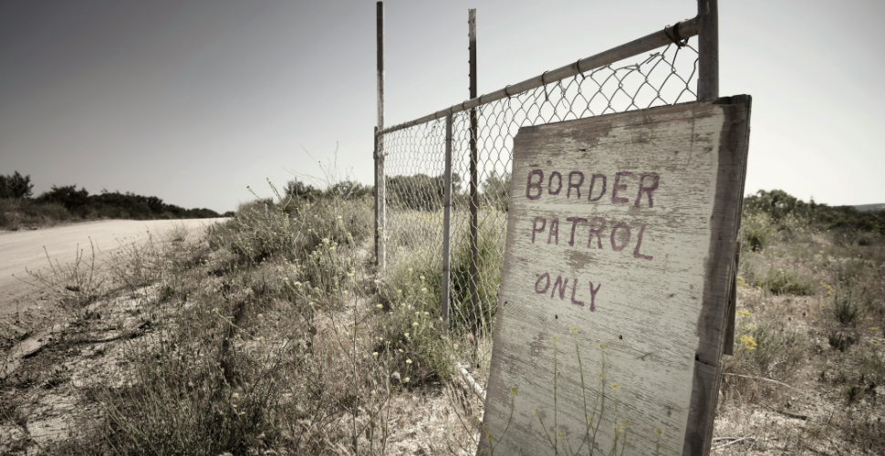 wooden board leaned up against a wired fence with the words border patrol representing the U.S. deterrence policy.