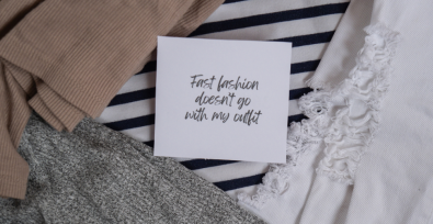 Citazione "il fast fashion non va bene con il mio outfit" su un pezzo di carta sopra vari capi di abbigliamento