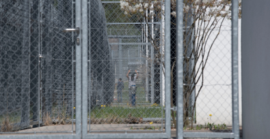Persona detrás de una valla metálica en un centro de detención de inmigrantes
