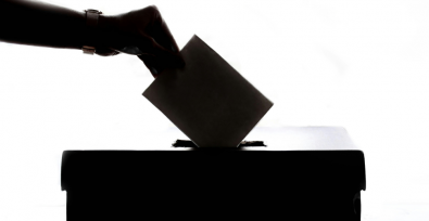 silhouette of a hand submitting a ballot into a ballot box