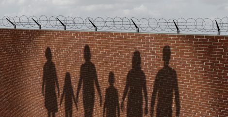Shadow of figures holding hands projected on a brick wall with barbed wire