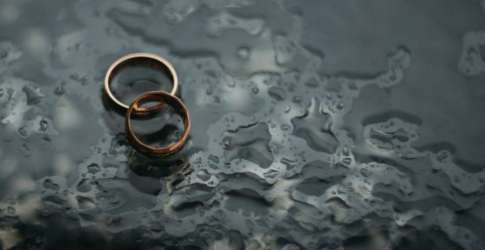 twe metal wedding bands resting together on a water splattered dark glass surface
