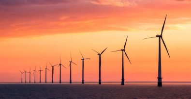 A long row of wind turbines standing against a sunset sky