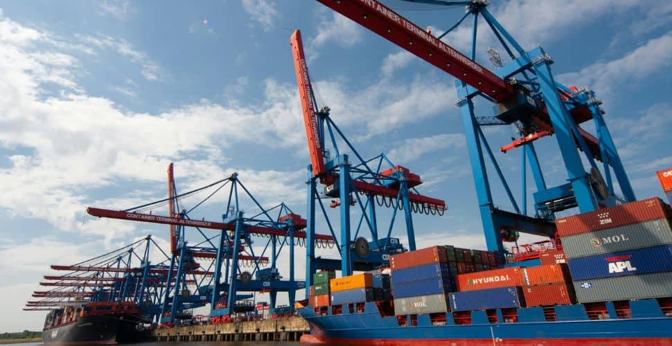 Cranes loading containers onto ship against blue sky