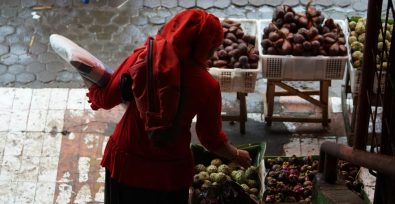 Eine verschleierte Frau prüft Obst auf einem Markt.