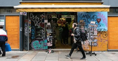 London shop with graffiti covered front and a man walking by