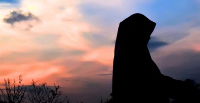 silhouette of woman in hijab against orange and blue sunset